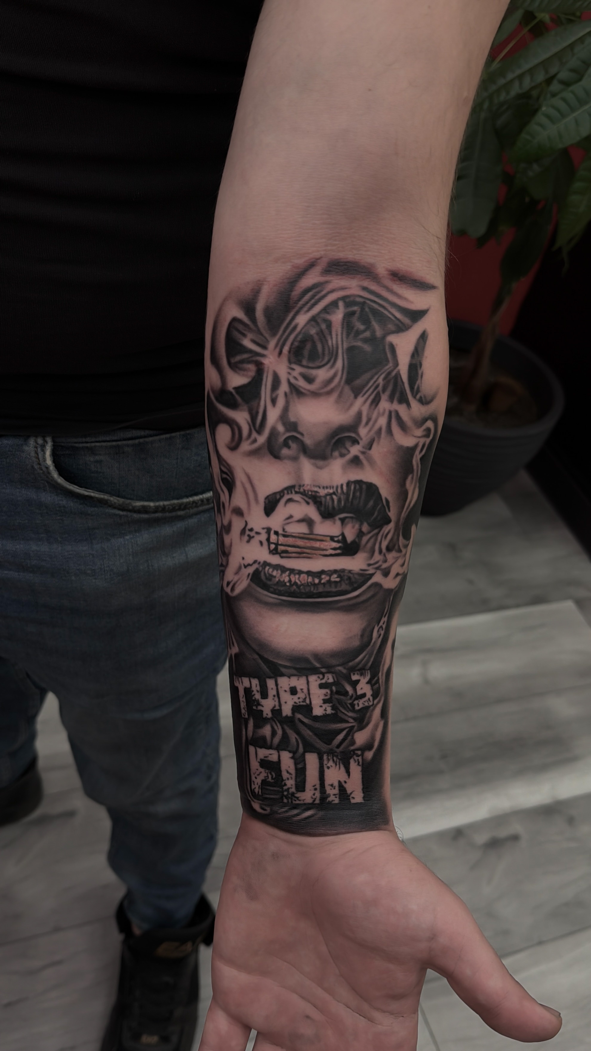 Tatuaj black & grey cu mască și personaj pe antebraț